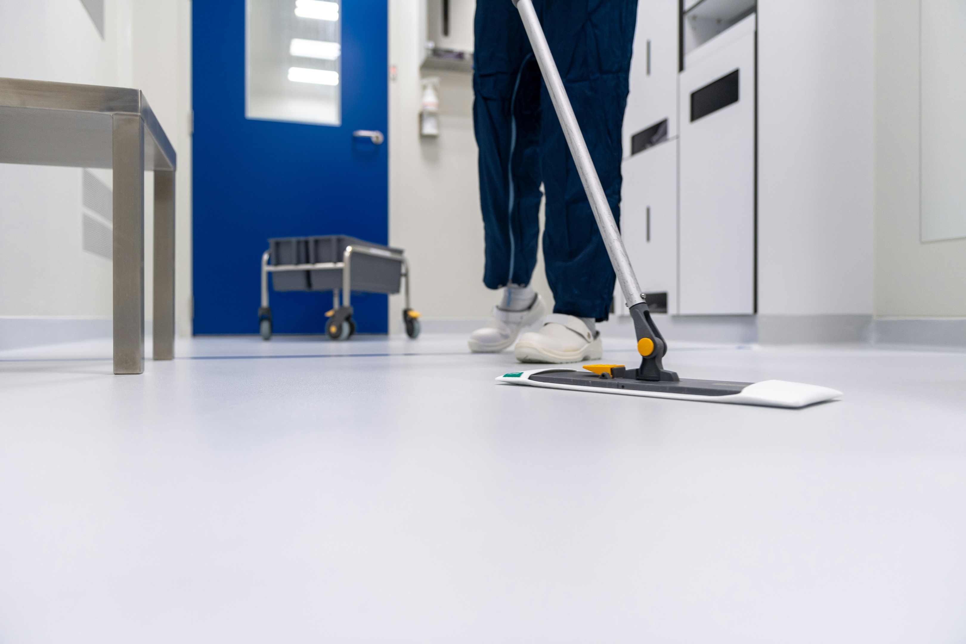 A person wearing yellow gloves is operating a floor cleaning machine in a bright, modern workspace.
